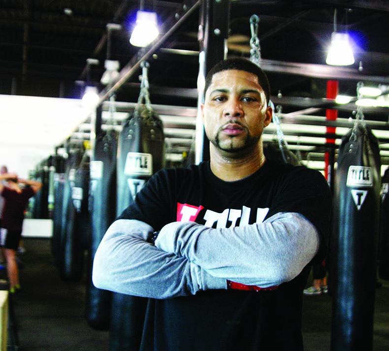 Crossing his arms, security guard Arnold Enclarde poses in front of punching bags at Title Boxing Club, where he teaches a boxing class three days a week.