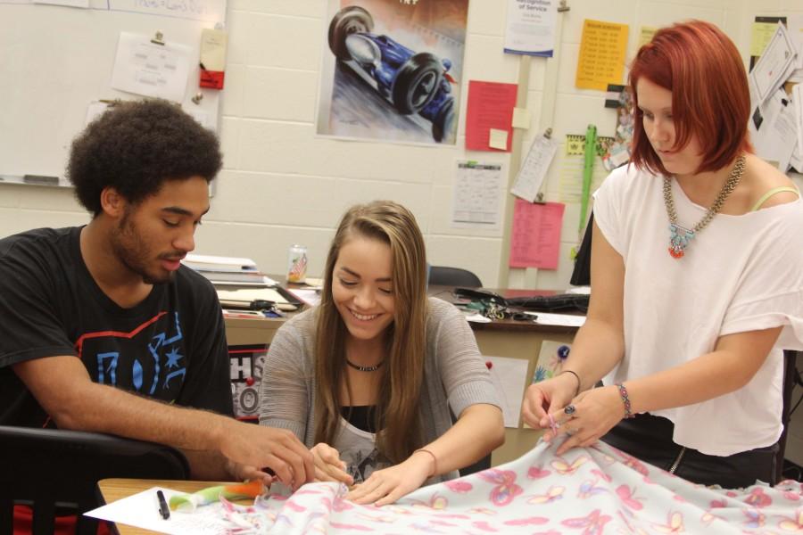 Working with fabric, junior Bronxton McGee, sophomore Monica Marin Steffes, and senior Emily Laughlin create a blanket for a child in need during the Oct. 28 Project Linus meeting.