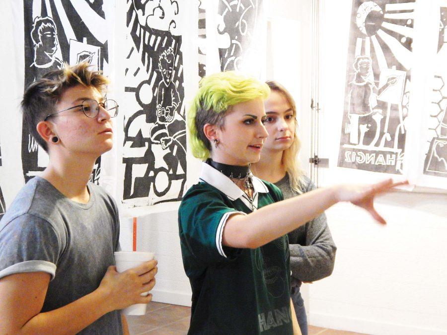 Observing the Art — Senior Toby Weston explains a woodblock carving that Hang12 members made for a recent show to junior Mia Romano and sophomore Olivia Rothrock. 