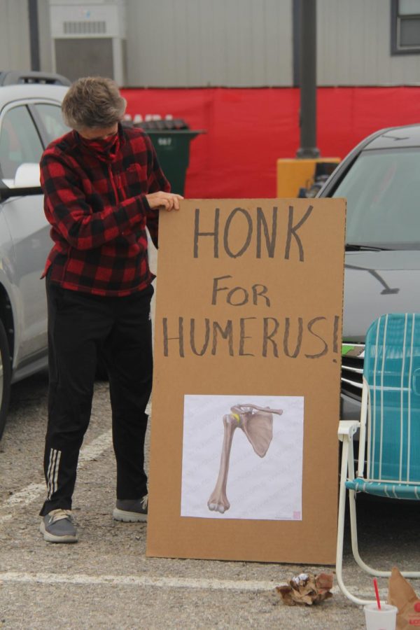 Jo Huntsinger proudly displays her Honk for Humerus sign for the senior class as seniors picked up caps and gowns on Thursday in the LHS parking lot. Huntsinger is retiring this year.