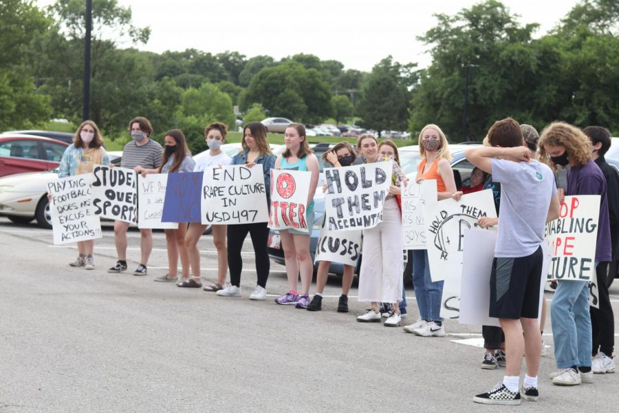 Students stand outside the district holding signs calling for action on sexual assault in schools at the June 28 board meeting.