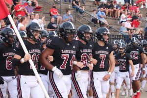 LHS football players link arms as they walk out for the first football game of the season Sep. 2 against Olathe East.