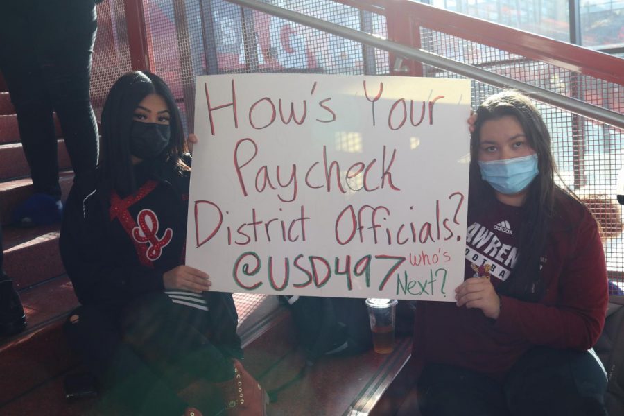 Seniors Donna Gonzalez de la Rosa and Leia Poettker hold a sign critical of district administration salaries as the district contemplates eliminating girls gymnastics.