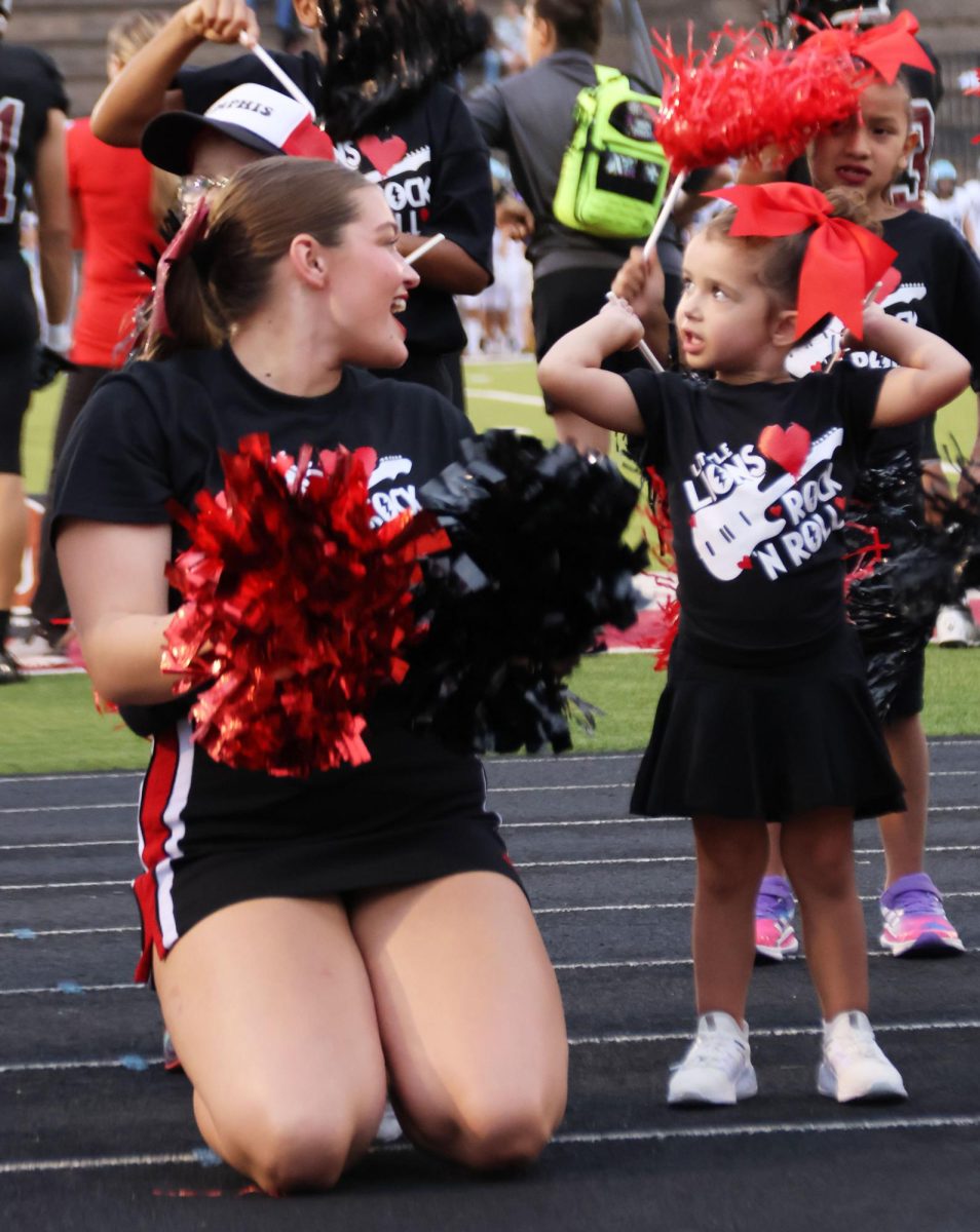 Senior Charlee Burghart cheers with a Little Lion participant at the home football game on Sept. 15th.