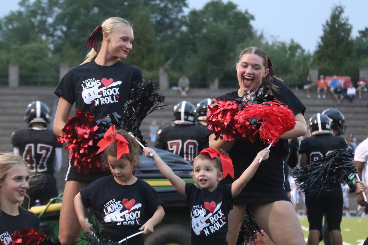 Senior Charlee Burghart dances and junior Nora Steinle dance with Little Lions participants on the sideline at the home football game on Sept. 15 against Shawnee Mission East.