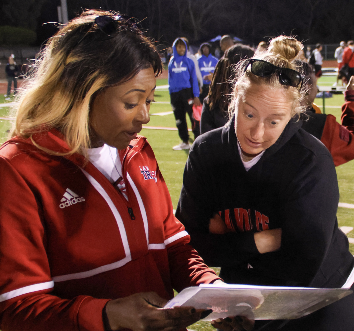 Comparing times, head track coach Audrey Trowbridge excitedly talks with coaches Laura Brensing and Kyle Morgison after the 4x4 relay on April 12.  