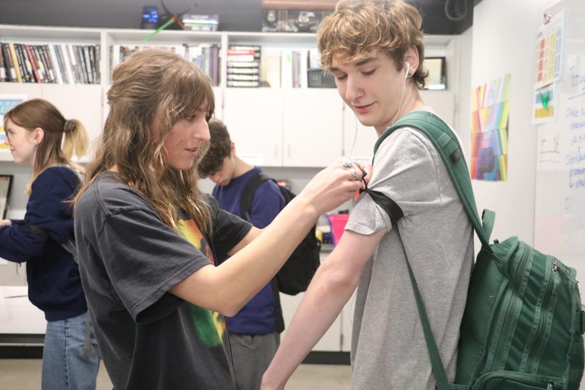 Junior Ava Lee, a member of the journalism staff, ties an armband on a classmate as journalism students worked to build support for concerns around Gaggle. Students wore armbands on March 29 as a group of editors met with district administrators about their concerns.