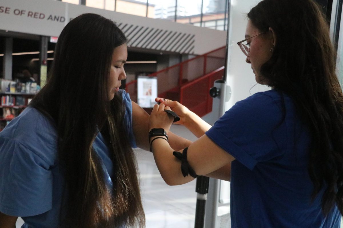 Tying a black armband, junior Arabella Gipp helps build support for journalism staff concerns on March 29. At least 320 armbands were worn by students and staff at Lawrence High and Free State.