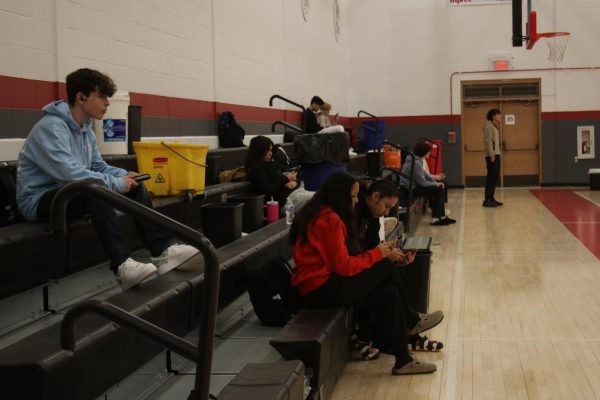 Students sit in the bleachers of the west gym, which has been the home to a number of water catching buckets since January.