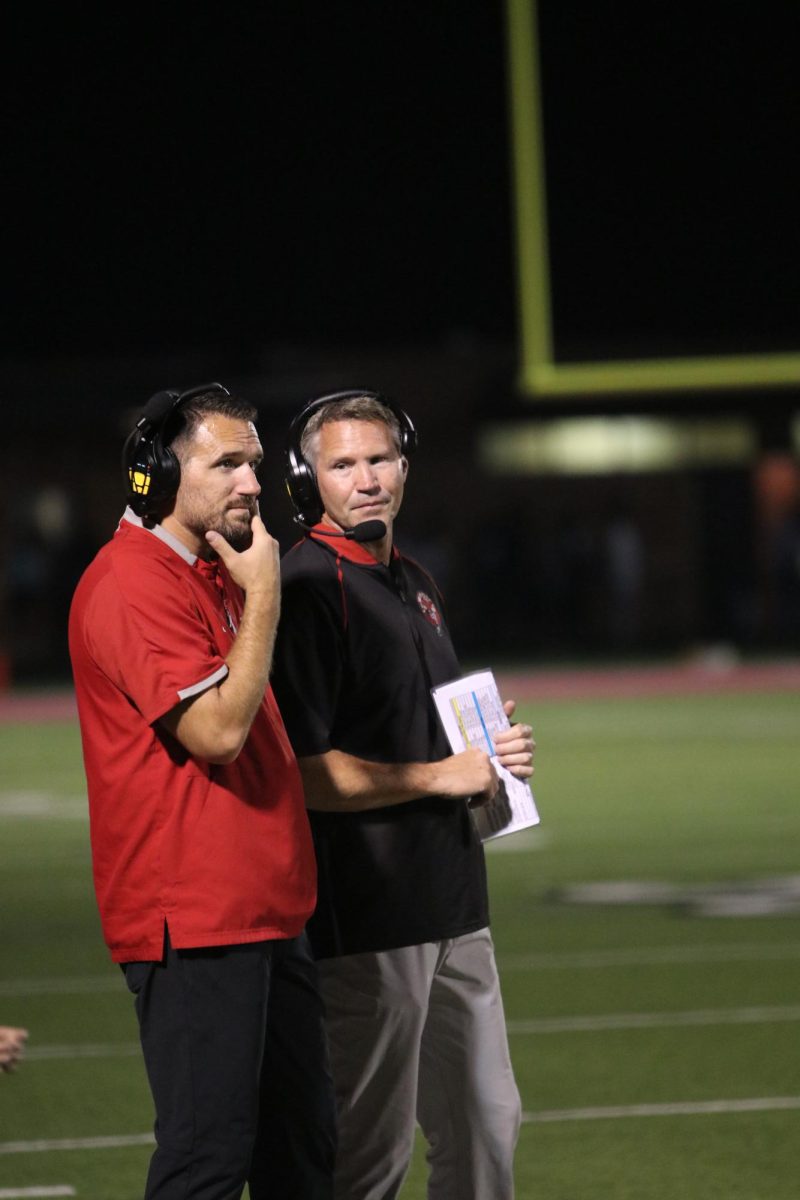 Talking on the sidelines, Bowen discusses plays with assistant coach, Taylor Stuart during the game against Shawnee Mission West on Oct. 4th. The Lions won 55-0